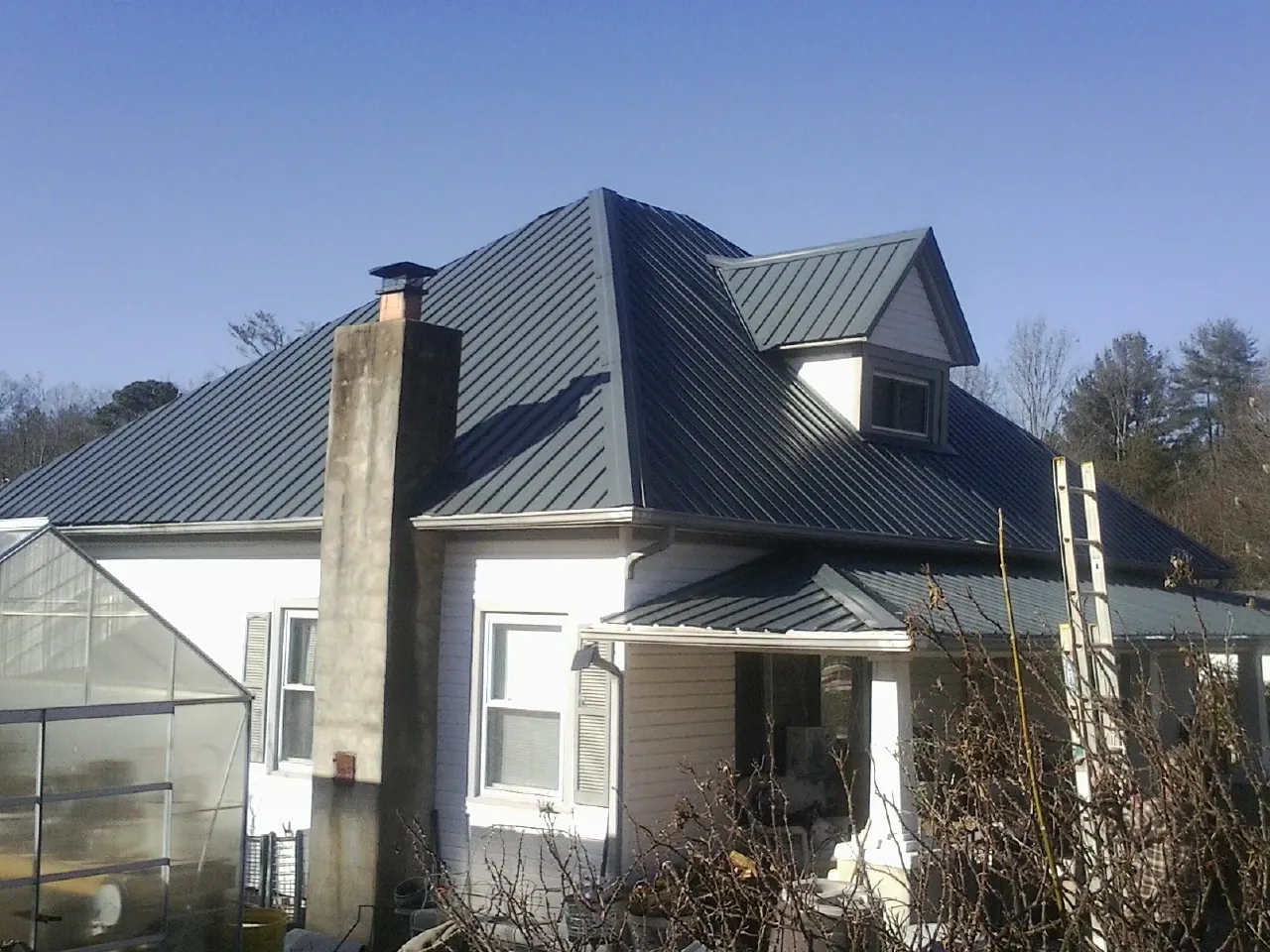 Dark blue standing seam metal roof on a white farmhouse with dormer — Slate & Tile Roof Repair by Roofing Brothers in Mount Blanchard
