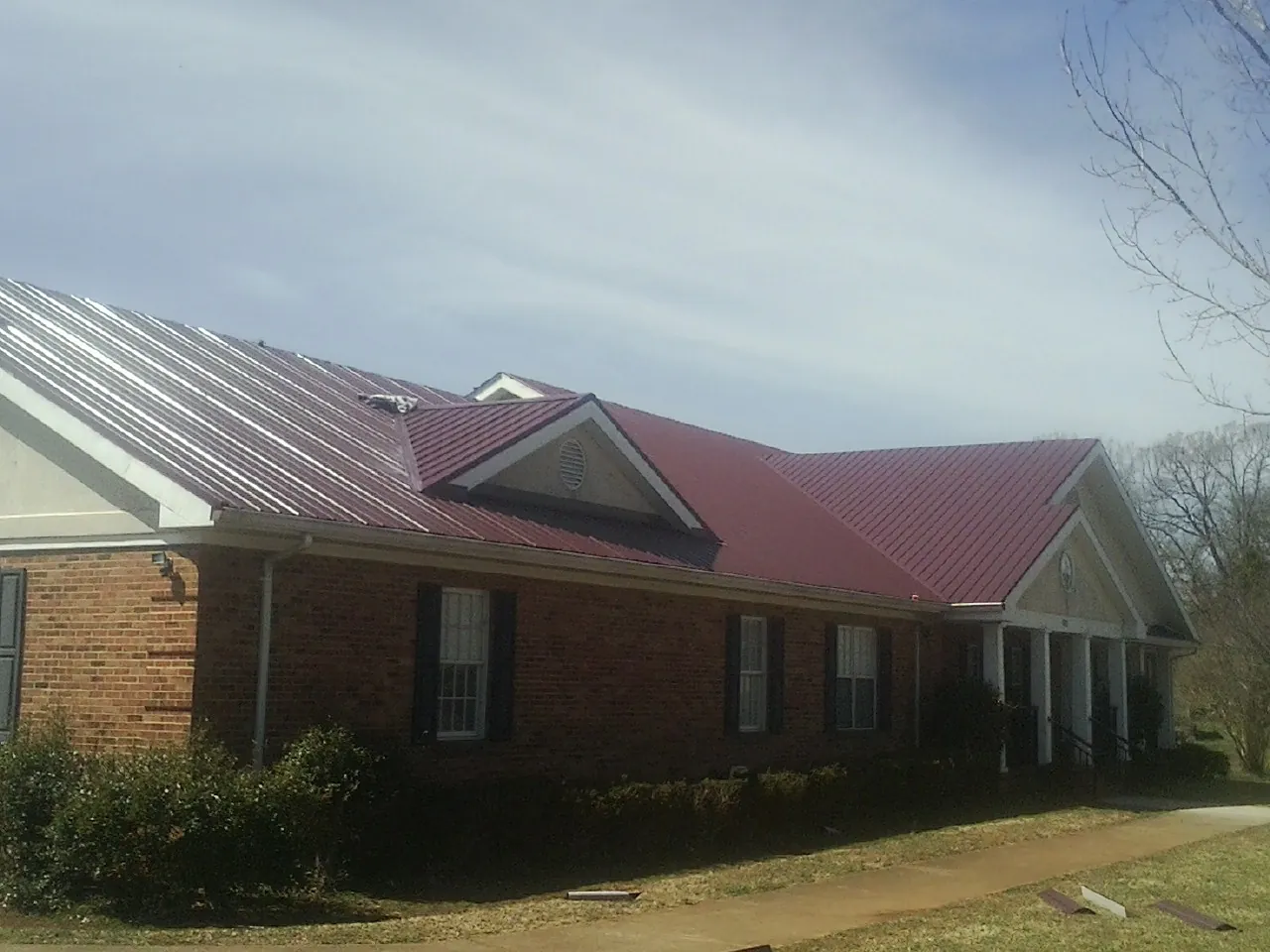 Red metal roof with gabled entries on a long brick building, from a Hail Damage Roof Repair job in Mount Blanchard