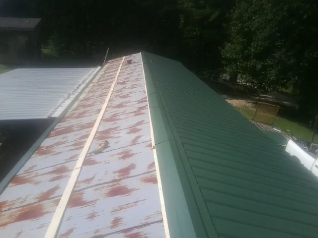 Old rusted panels beside newly installed green metal roofing — Wind Damage Roof Repair by Roofing Brothers in Mount Blanchard