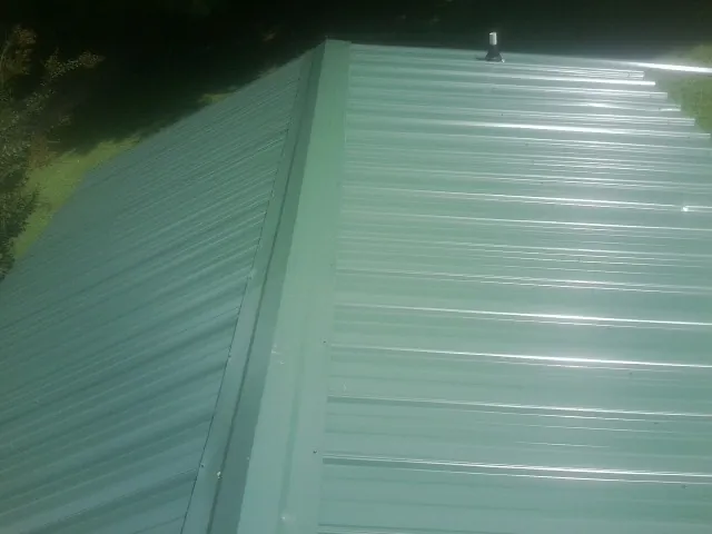 New green metal panels meeting at the ridge of a roof — Flat Roof Repair work by our crew in Mount Blanchard