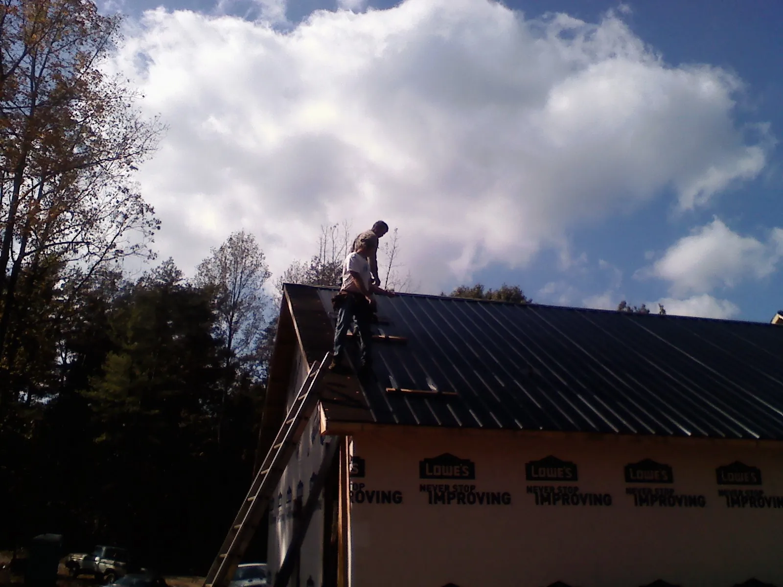 Roofer fastening dark metal panels high against a cloudy sky, from a Roof Inspection job in Mount Blanchard