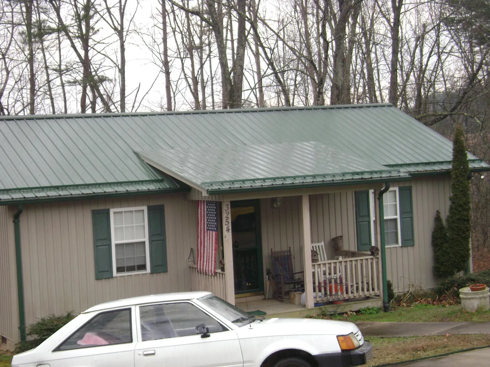 Green metal roof and front porch on a tan sided cottage in Mount Blanchard