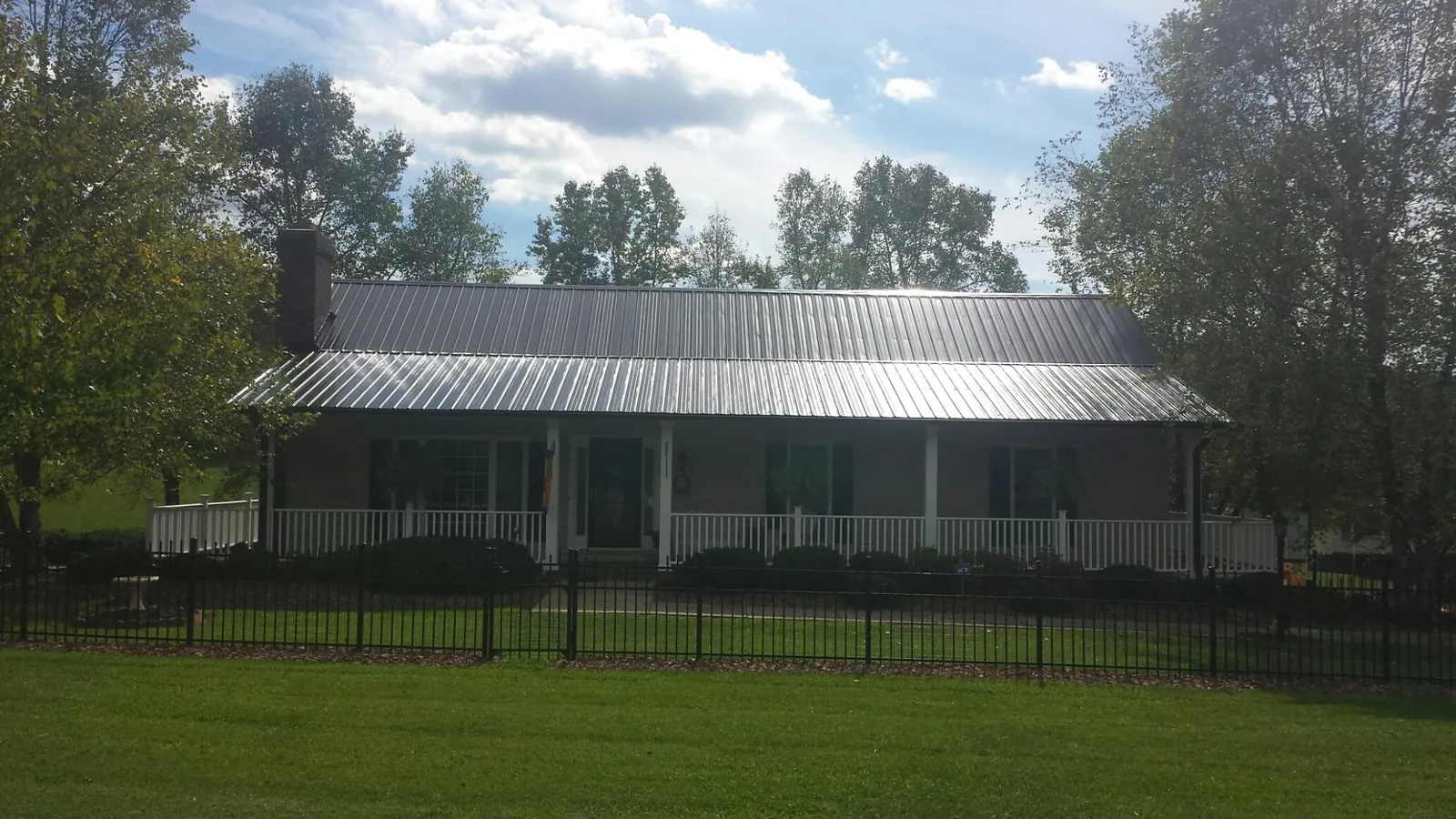 Gray metal roof on a brick ranch with a full width front porch — Gutter Guard Installation work by our crew in Mount Blanchard